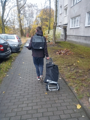 Człowiek idący po chodniku z torbą na wózku - w torbie ulotki do rozdawania